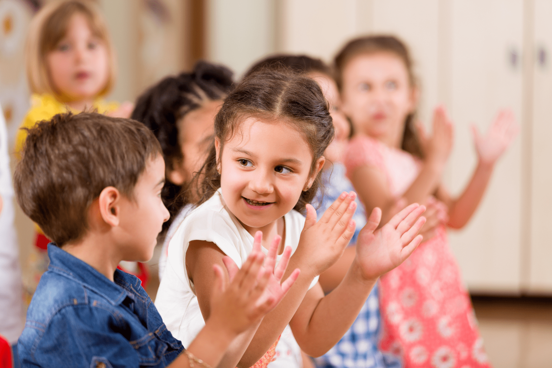 Children clapping and smiling in a preschool classroom.