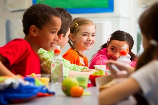 Two girls and Two boys sitting at a table talking and eating lunch.