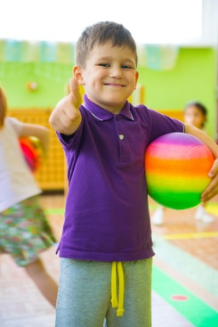 Little boy holding colorful ball giving a thumbs up.