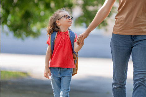 A Preschooler walking to school holding mom’s hand smiling.