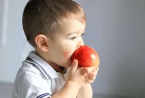 A Two-year-old eating a red apple with both hands.
