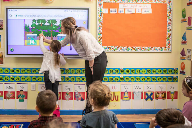 Teacher assisting child to complete lesson on the smartboard.